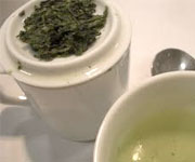 Close-up of green tea in a cup and tea leaves on a caddy.