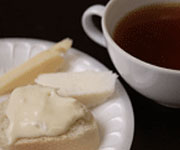 A cup of tea next to a plate with bread and cheese.