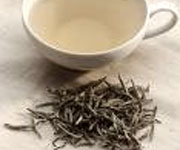 White tea in a teacup with a sample of loose-leaf white tea next to it.