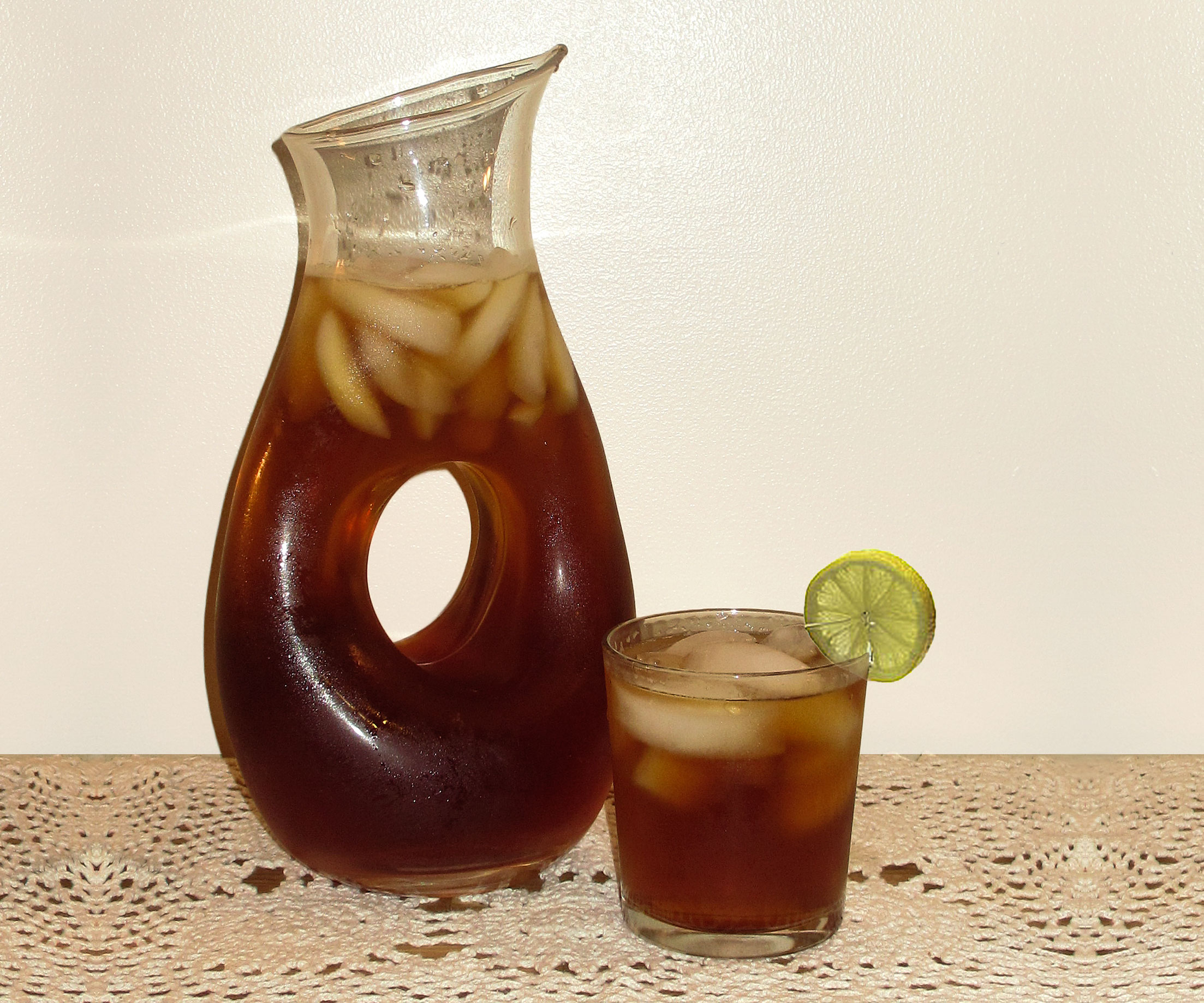 Pitcher of iced tea next to a short glass filled with iced tea.