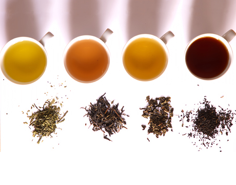 Four cups of different teas with samples of loose-leaf tea on table next to them.