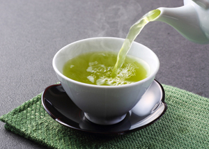 White teapot pouring green tea into a teacup.