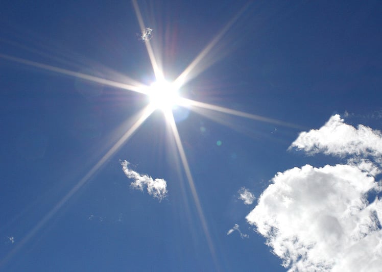 Sun in a blue sky with puffy clouds.