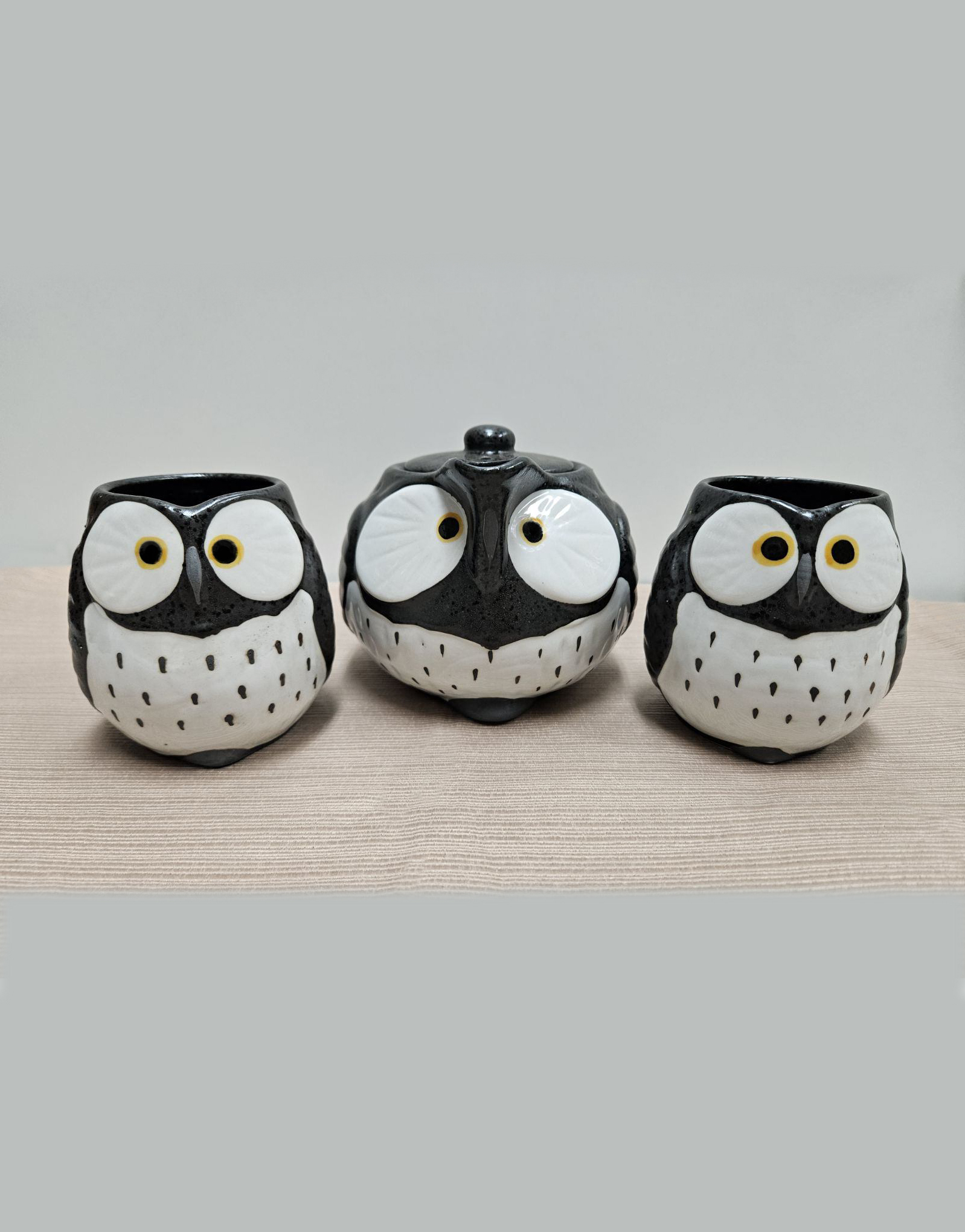 Small owl-shaped teapot and two owl-shaped teacups, black with white bellies.