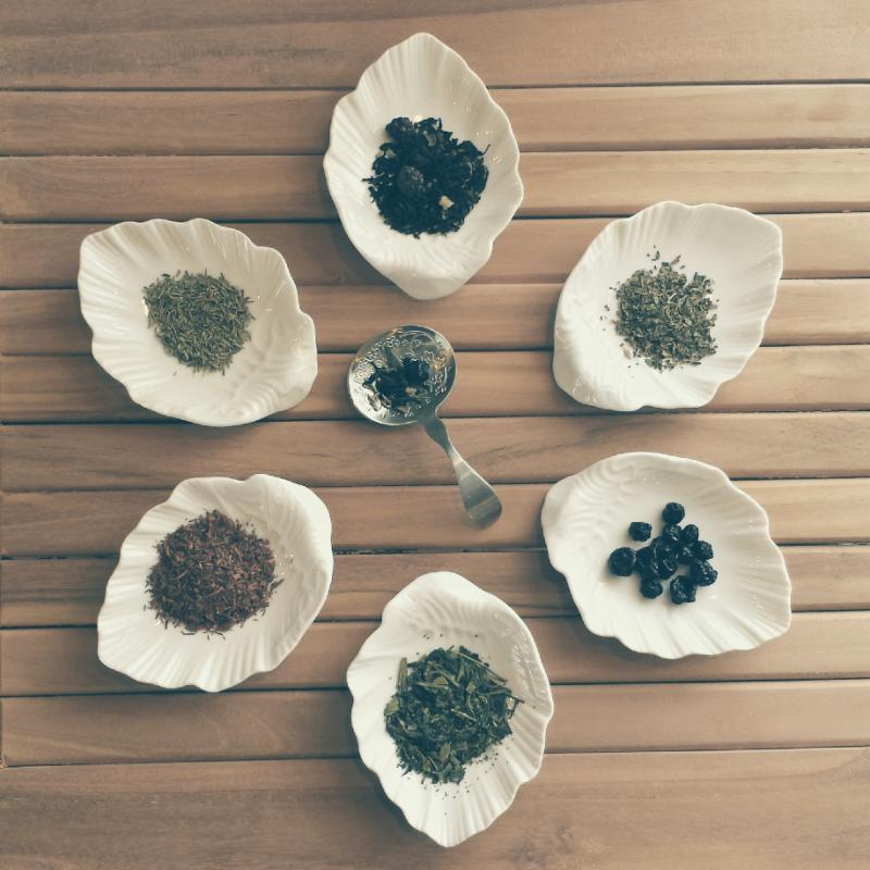 Six white ceramic leaf-shaped tea caddies, each holding a small amount of different teas.